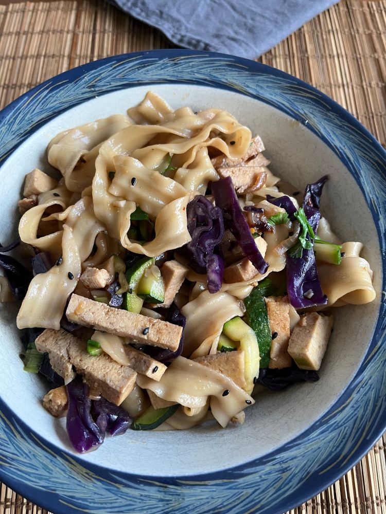 A blue bowl of ruffle-y noodles with veggies. 