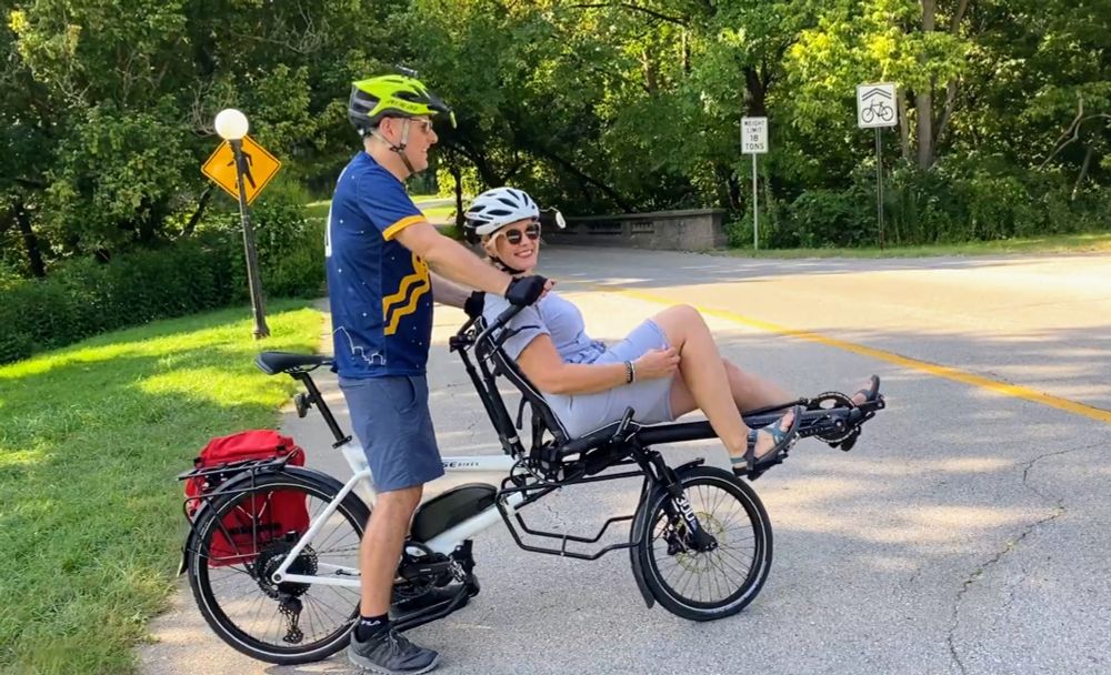 Two people about to ride a tandem bicycle with the front person recumbent