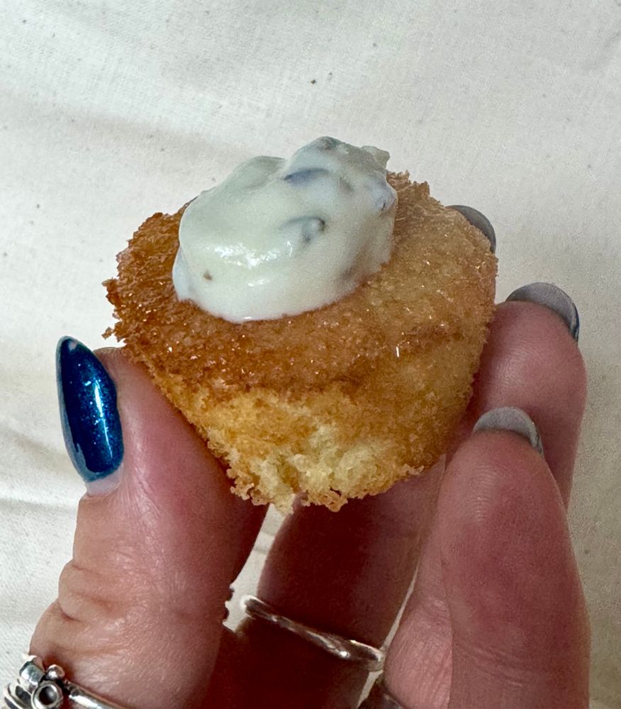 Ida's fingers gently cradling a tiny cake, soaked in bergamot drizzle and topped with a teeny quenelle of lavender cream.