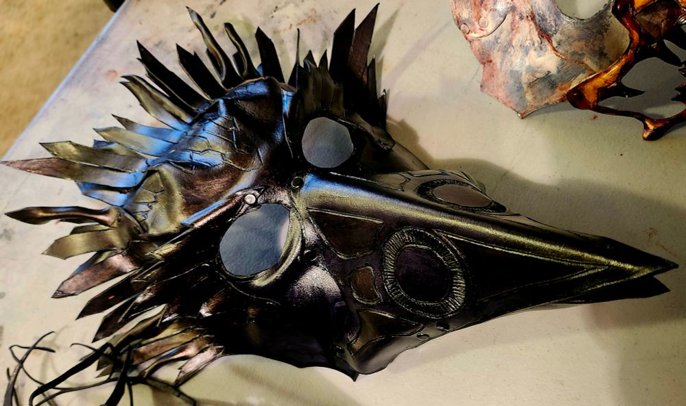 A black leather mask of a raven in a plague doctor style with heavily carved in details. 