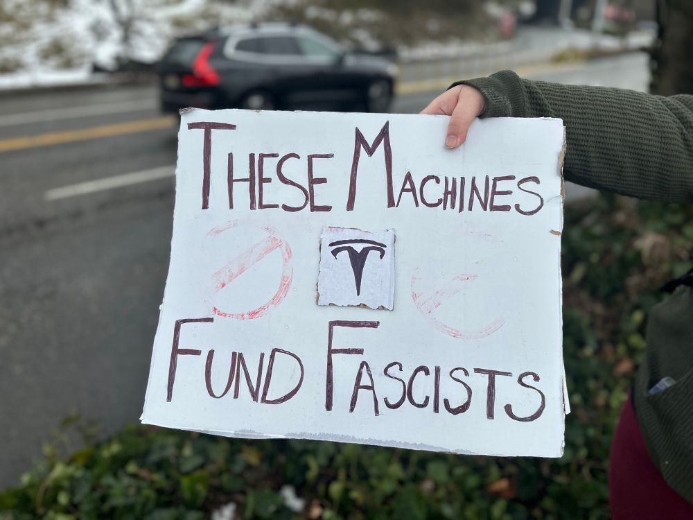 Sign: these machines fund fascists with a Tesla logo in the center 