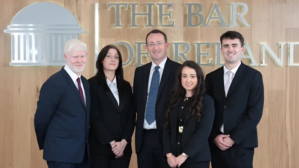 UL student Lee Mac Cuinneagain, Greta Baronaite of ATU Letterkenny, Bar Council chair Seán Guerin SC, Alvena Sharma of Trinity College Dublin and Michael White of University College Dublin. They are all dressed formally in suits and are standing in front of a sign on a wood panelled wall that says 'The Bar of Ireland'. (Photo credit: Robbie Reynolds Photography)