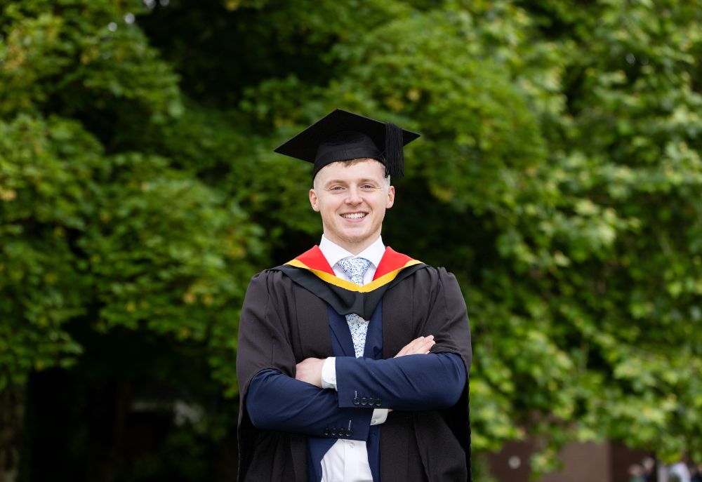Picture of a man in graduation robes in outdoor setting