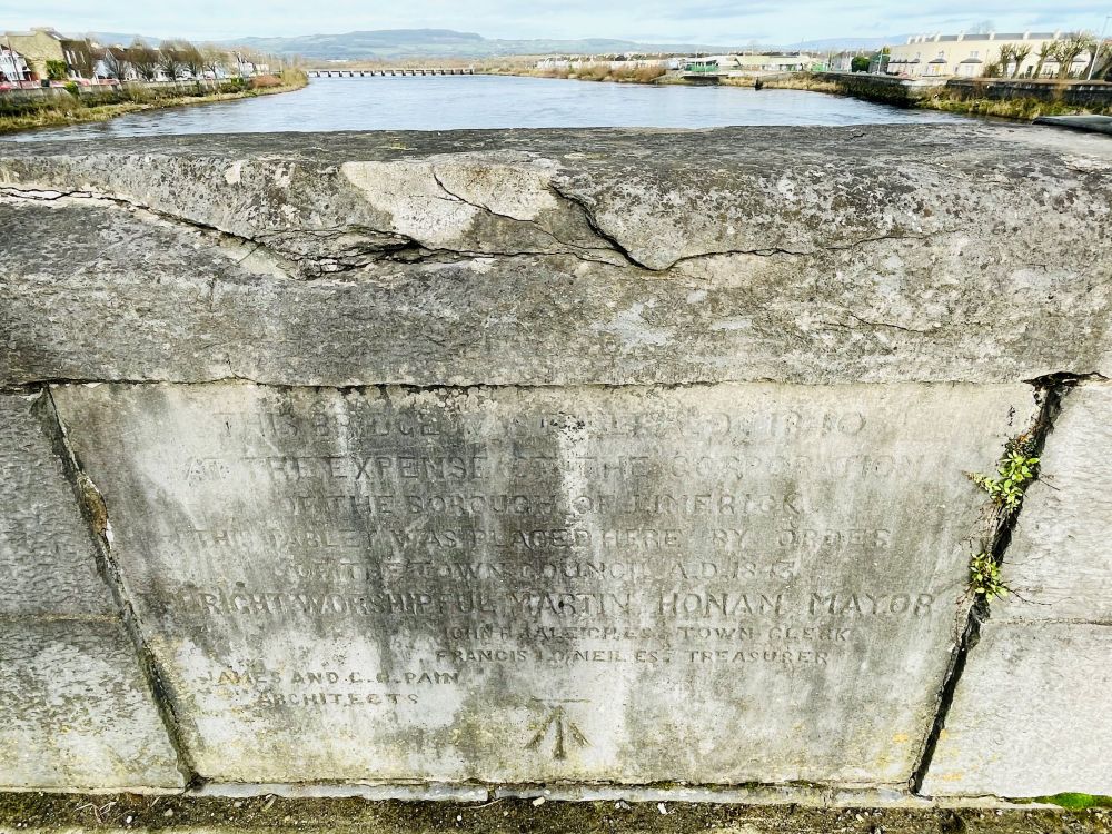 A photo of a large old piece of masonry with markings and faded writing on it, with a body of water in the background