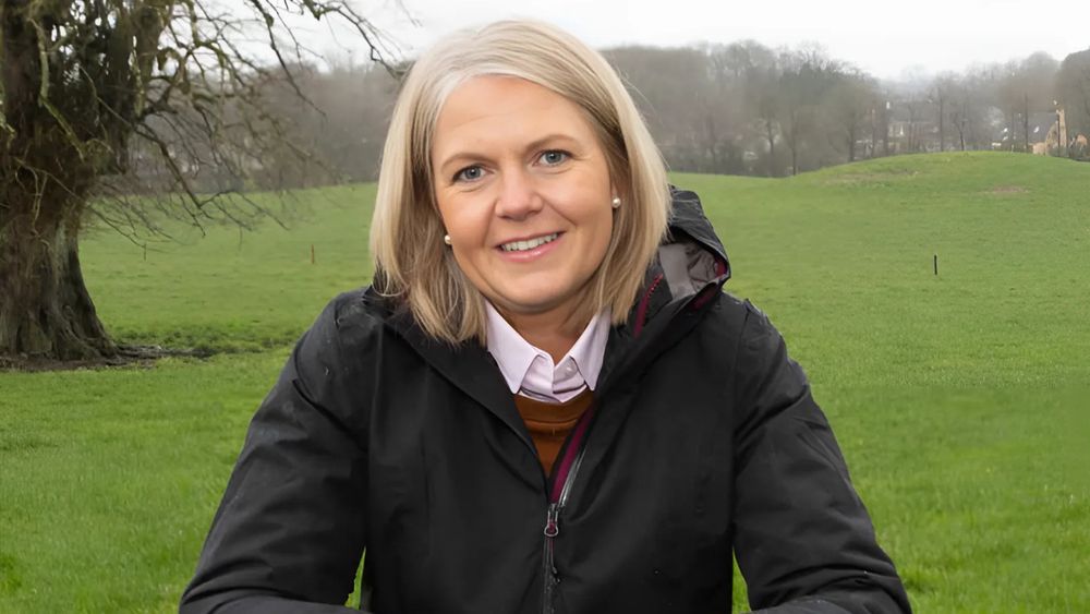 UL graduate Aisling Meehan. She has shoulder length blonde hair and is wearing a black rain jacket. She is standing in a field with a large tree in the background. 