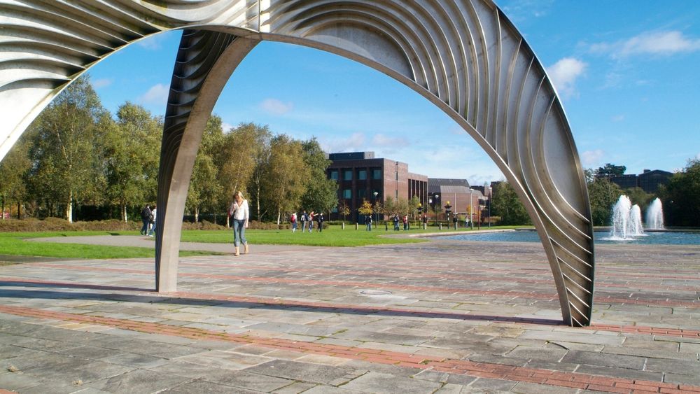 A photo of a university campus, with people walking, through the lens of a metal art sculpture