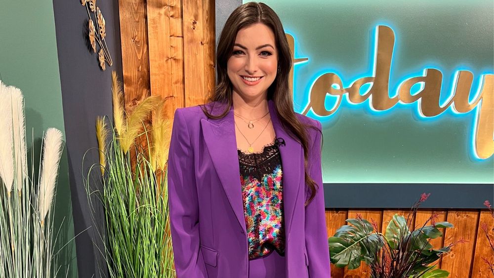 A photo of a woman in smart dress, standing in front of a screen featuring the word 'today'