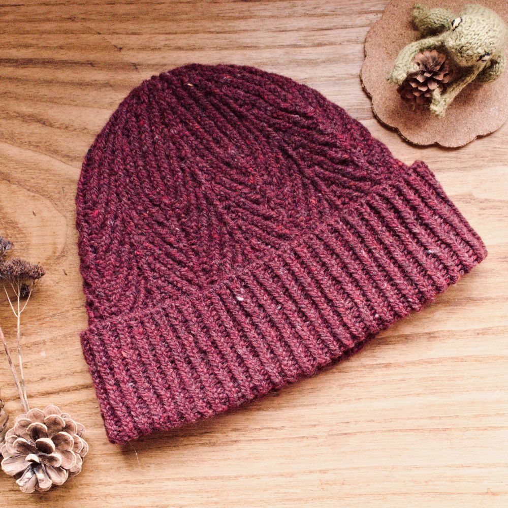 Red hand knitted Alatau Hat shown flat on a wooden table. It has been knitted in BC garn Loch Lomond yarn. 