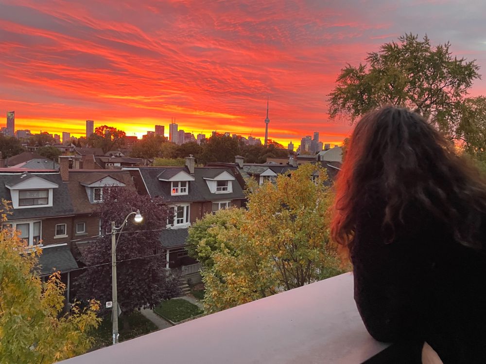 view of a sunrise and the Toronto skyline with a woman with curly brown hair in the foreground