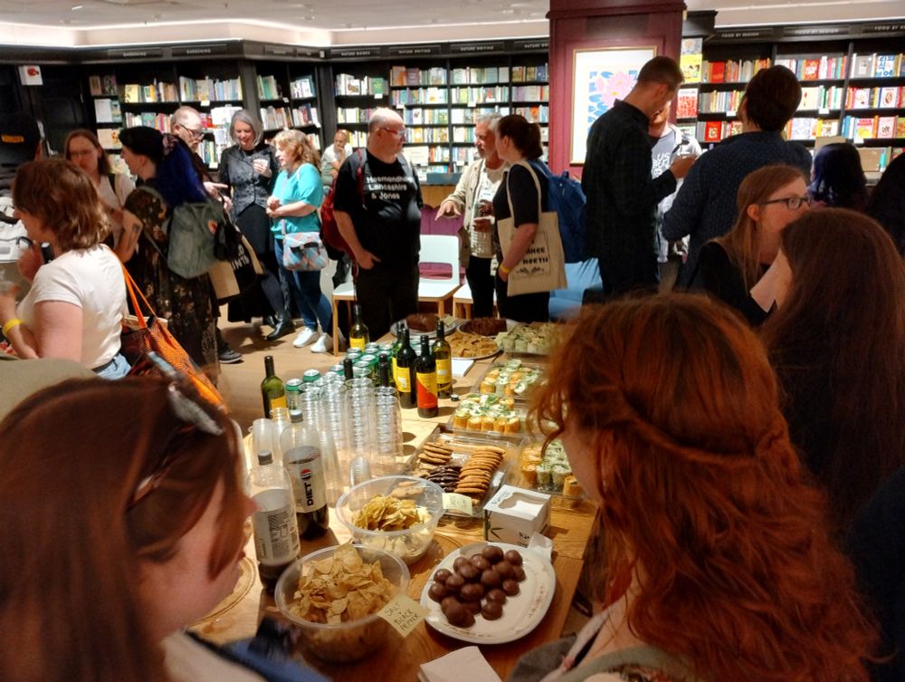Readers and authors mingling with food and drink on a table in the middle