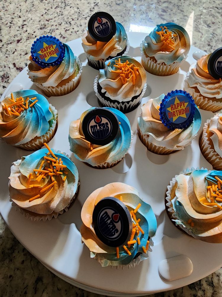 Photo of cupcakes with orange and blue icing, and Oilers charms on top.