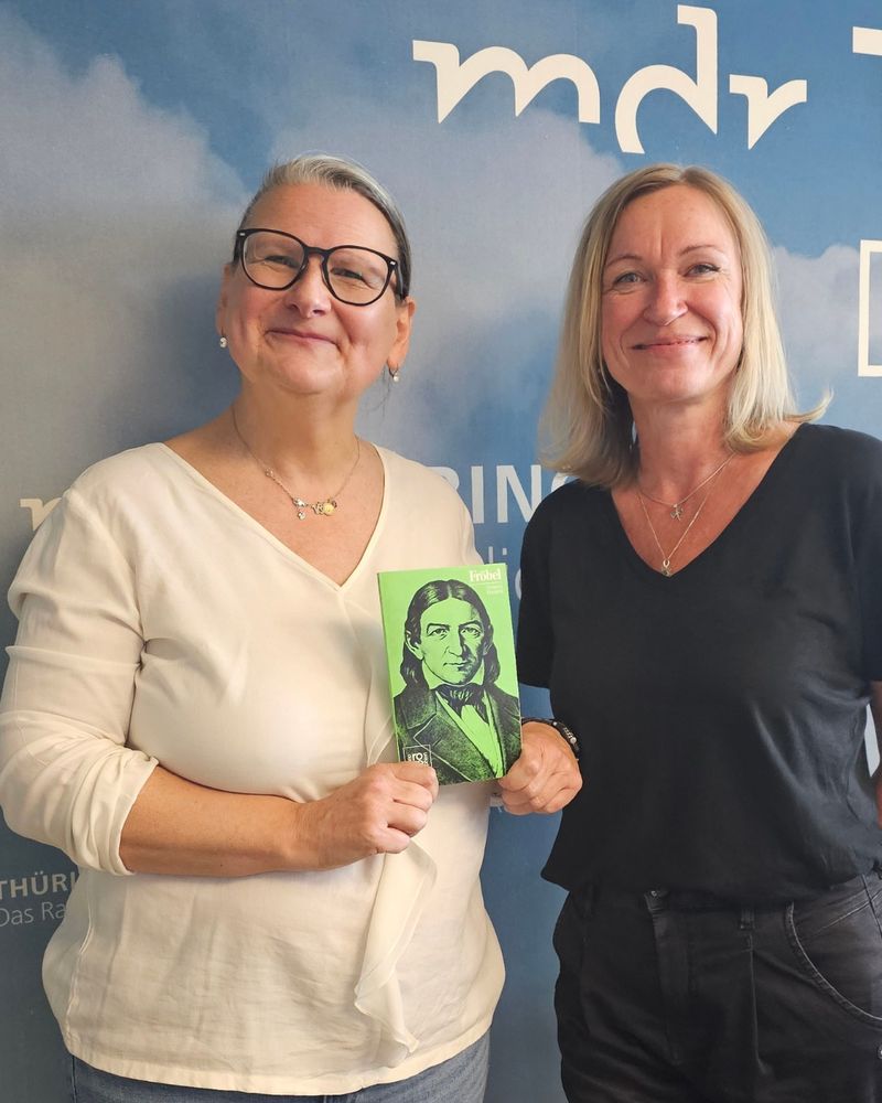 Zwei Frauen lächelnd in Kamera, links mit Fröbel-Buch Prof. Dr. Andrea C. Schmid der Universität Erfurt und rechts Sina Waage, Moderatorin beim MDR, oben rechts MDR-Logo