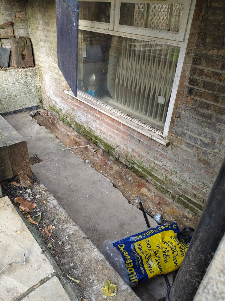 An image of a wall with a shallow trench dug to reveal part of the foundation 