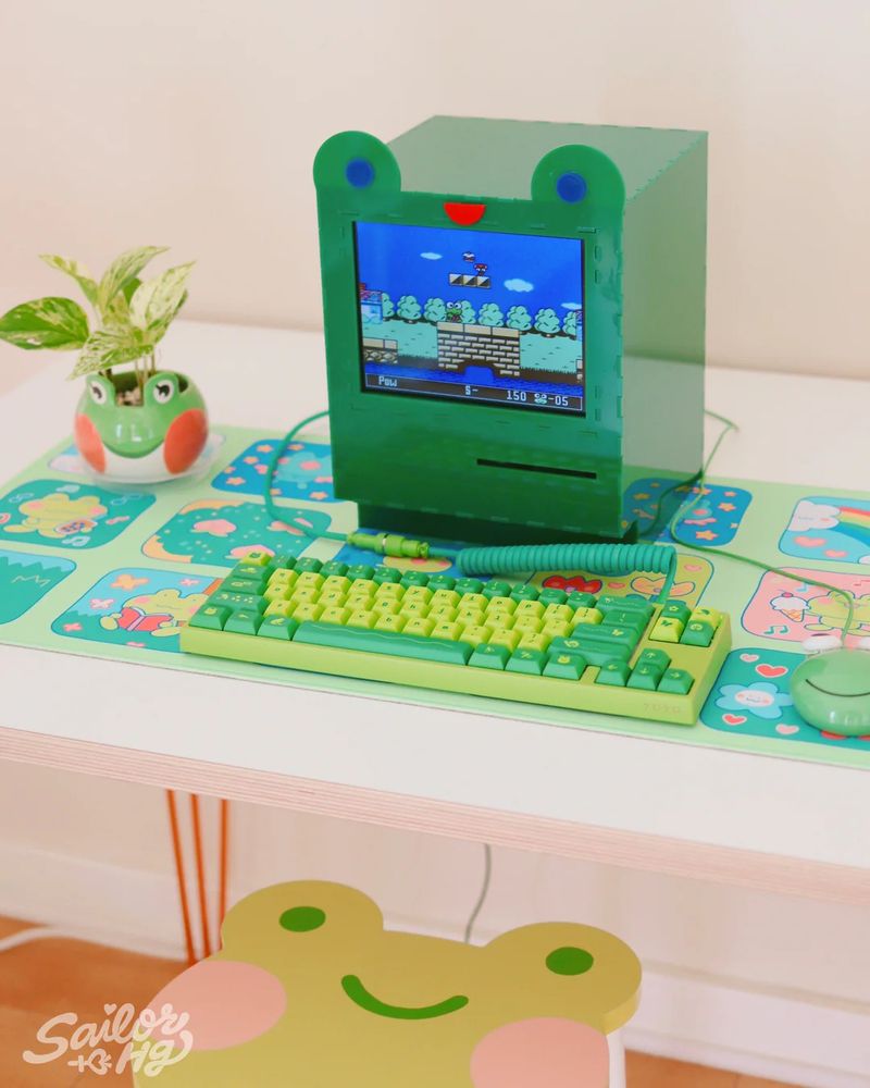 frog desk set up with frog shaped computer and green keyboard with frog keycaps, frog planter, and chair with a frog face