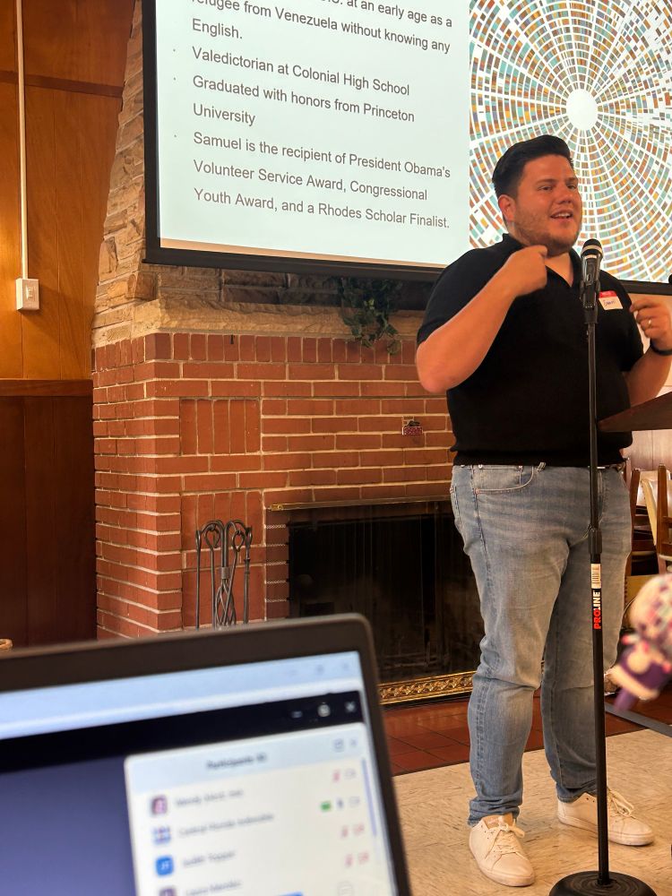 Samuel speaking in front of a fireplace. 