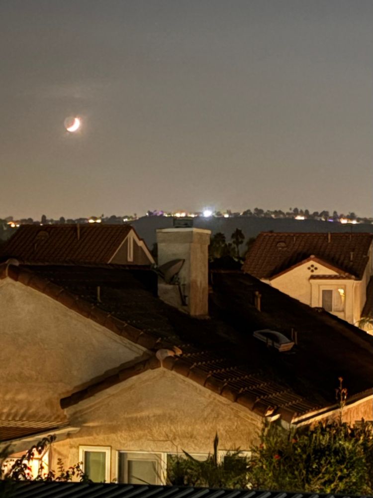 Waxing, crescent moon over red tiled roofs.