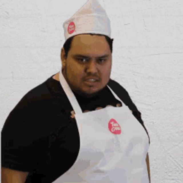 a man wearing a white apron and a white hat with a red logo that says tom 's crust