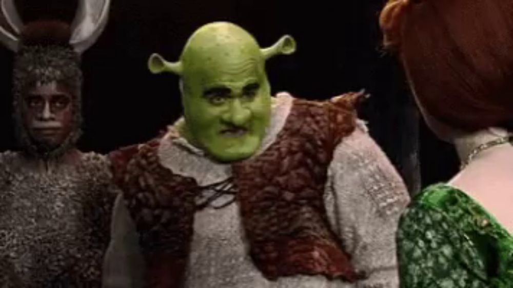 shrek is standing next to a woman in a green dress and a man in a costume .