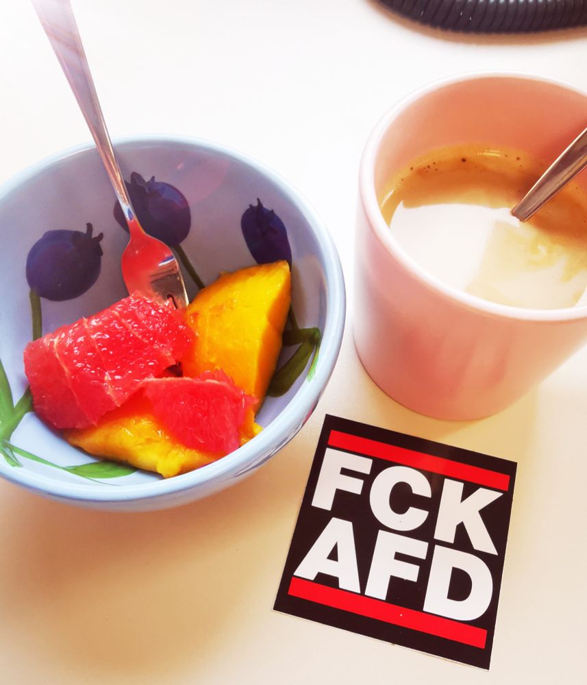 Ein Schälchen mit Mango und Grapefruitstücken, eine Tasse Kaffee und ein Sticker mit dem Aufdruck FCK AFD 
