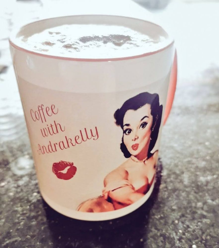 Tasse Kaffee mit Milchschaum und auf der Tasse ist mein Profilbild (Pinupgirl von Gil Elvgren) mit dem Schriftzug Coffee with Andrakelly und einem Kussmundabdruck darunter 