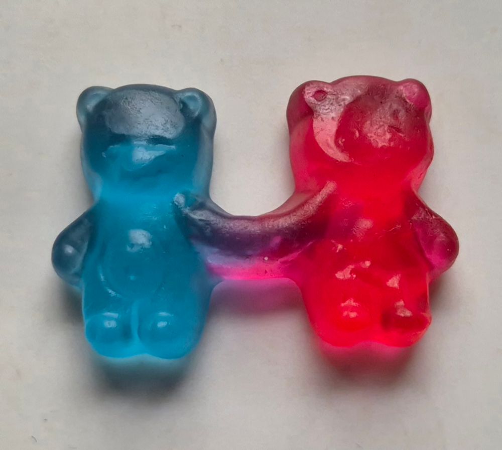 Zwei Gummibärchen, die sich die Hand geben. Eines ist rot, das andere blau. 