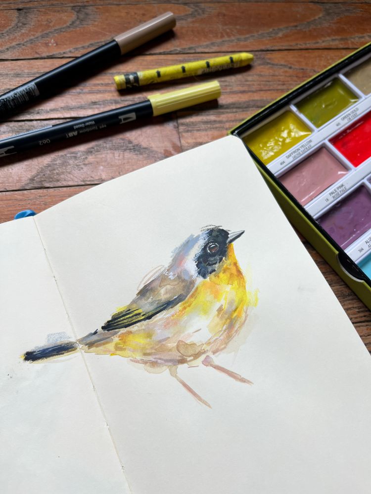 Sketchbook page featuring a mixed media painting of a male common yellowthroat with a bright yellow chest and black mask. 