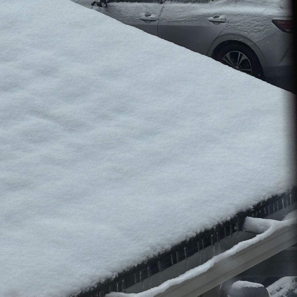 Snow on top of a roof with tiny icicles hanging down. 