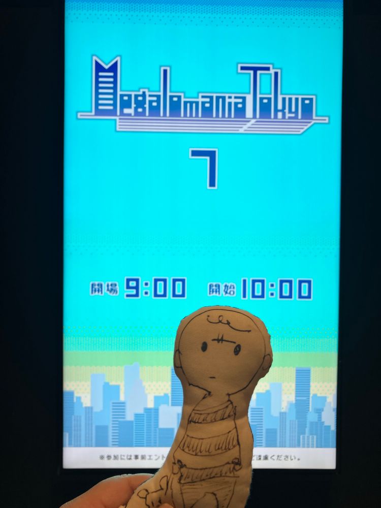 メガロマニアトーキョー7と書かれたデジタルサイネージの前に綿でできたぬいぐるみの「ぽけじょんちゃん」と。