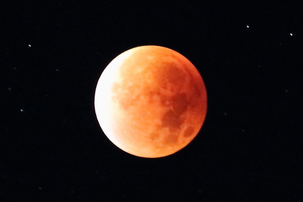 Käsefarbener Vollmond auf schwarzem Hintergrund, der nur durch ein paar Sterne verziert wird.