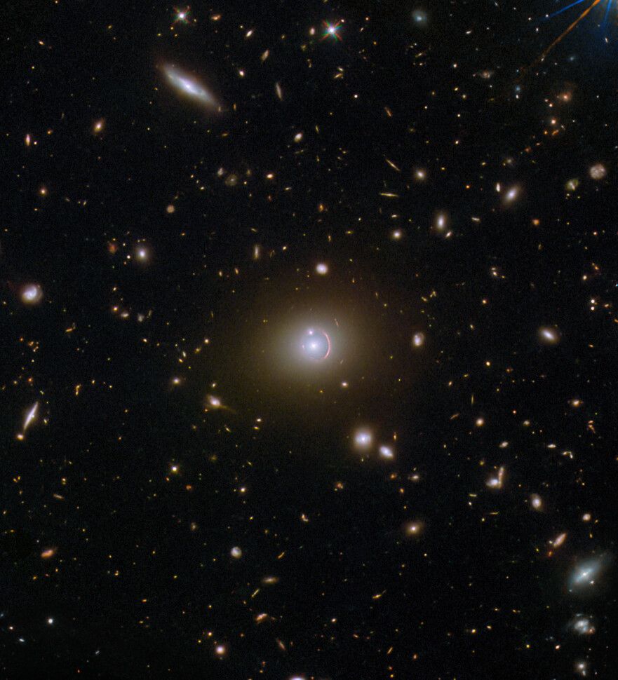 A field full of distant galaxies on a dark background. Most of the galaxies are very small, but there are a few larger galaxies and some stars where detail is visible. In the very center is an elliptical galaxy with a brightly glowing core and a broad disk. A reddish, warped, ring of light, thicker at one side, surrounds its core. A small galaxy intersects the ring as a bright dot.

Image credit: ESA/Hubble & NASA, H. Nayyeri, L. Marchetti, J. Lowenthal