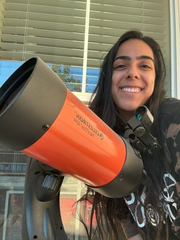 A selfie of me smiling next to my orange Celestron telescope.