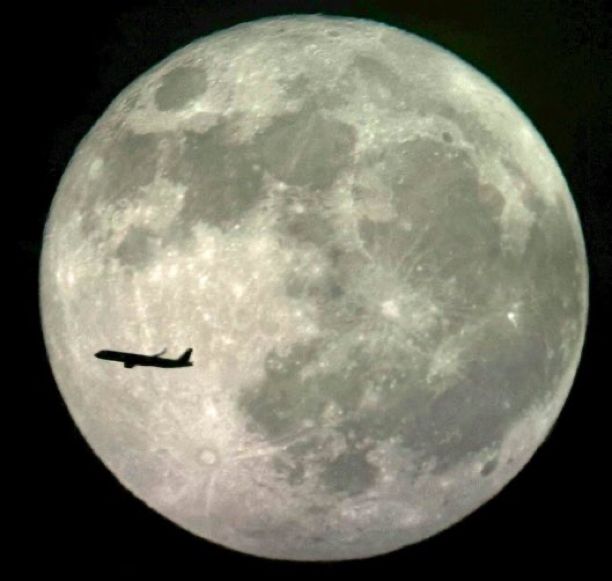 An airplane passing over the Full Moon.