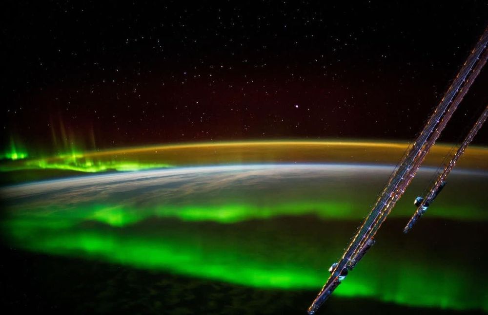 The green aurora can be seen above the Earth at night from the ISS. Many stars are visible in the background against the blackness of space.