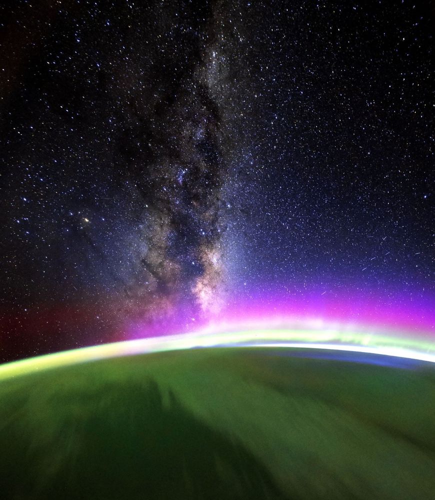 The Milky Way above the Earth from space. The green and purple aurora can be seen in the atmosphere. 
