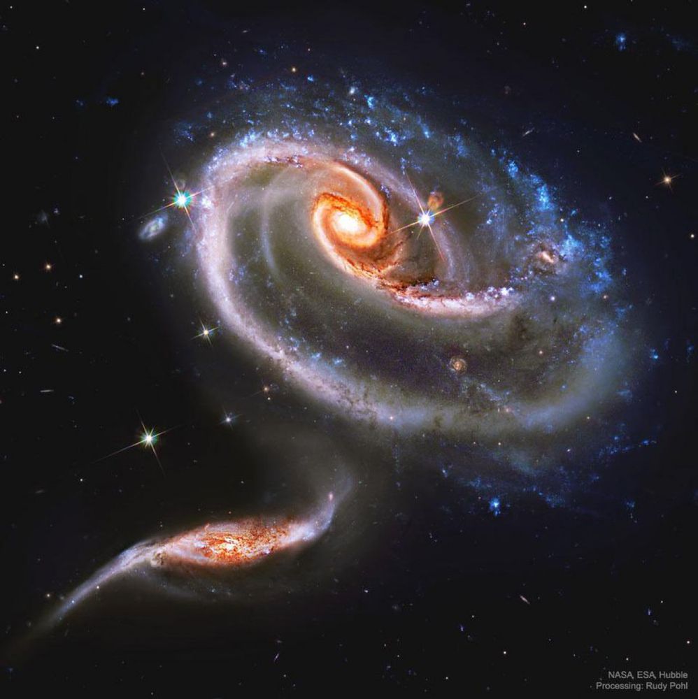 The upper galaxy is labelled UGC 1810 by itself, but together with its collisional partners is known as Arp 273. The overall shape of the UGC 1810 -- in particular its blue outer ring -- is likely a result of wild and violent gravitational interactions. The blue color of the outer ring at the top is caused by massive stars that are blue hot and have formed only in the past few million years. The inner part of the upper galaxy -- itself an older spiral galaxy -- appears redder and threaded with cool filamentary dust. A few bright stars appear well in the foreground, unrelated to colliding galaxies, while several far-distant galaxies are visible in the background.