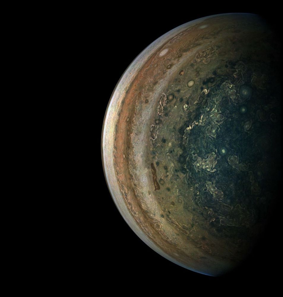 Jupiter’s hemisphere takes up the right half of the screen. As a color-enhanced image, its colors appear more saturated and richer, allowing the details of Jupiter’s swirls to be more defined. Jupiter’s stripes radiate from the center of the planet out, first in a deep teal, transitioning to a stripe of lighter green, followed by beige, terracotta, and beige once again.