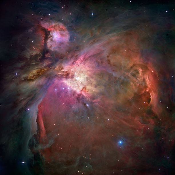 This expansive and cloudy cosmic landscape has sweeping clouds that shine in pink, yellow, orange, and brown. Some large, bright stars are visible glowing within the clouds and other foreground stars are peppered throughout the image.