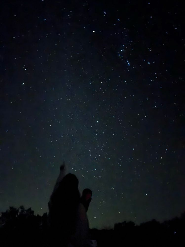 Me pointing to a starry night sky next to my telescope.