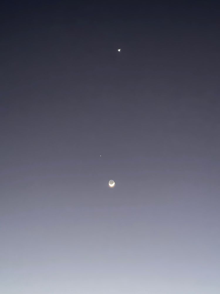 The Moon in the sky with two other bright dots which are Saturn and Venus. Saturn is to the upper right of the Moon and Venus is way above it.