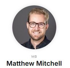 A head photo of Matt Mitchell, wearing a dark shirt and brown glasses