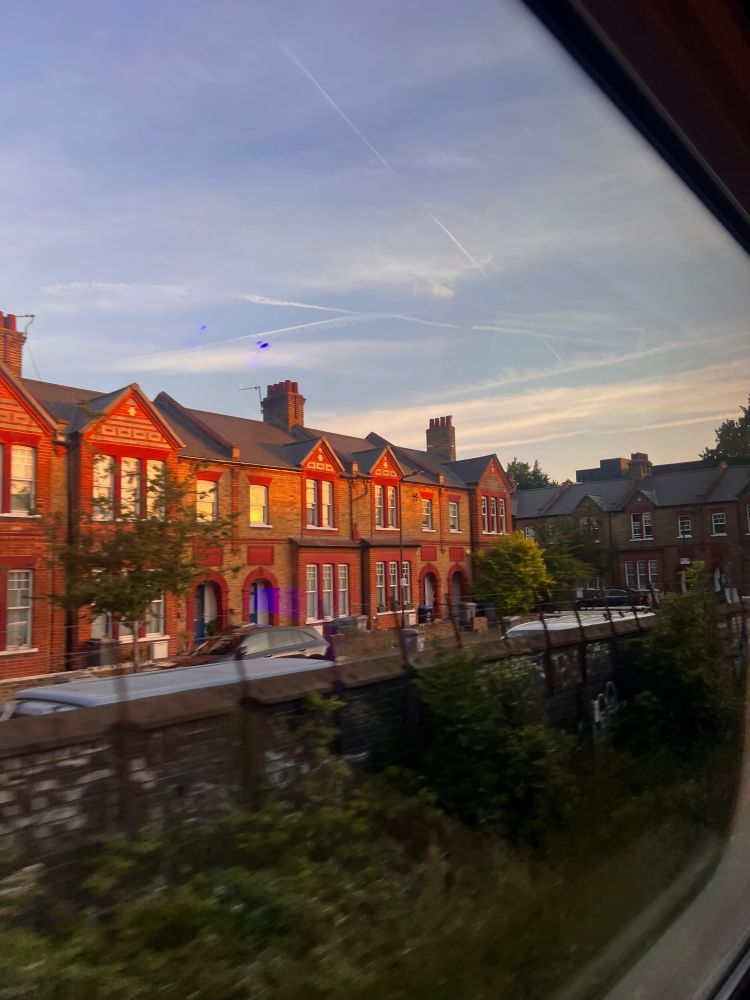Photo taken from the inside of a train out of the window showing tracks the sun setting over some houses 