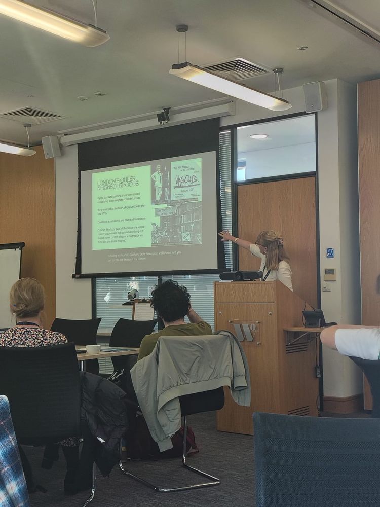 Woman standing behind a podium giving a talk and pointing at the screen 