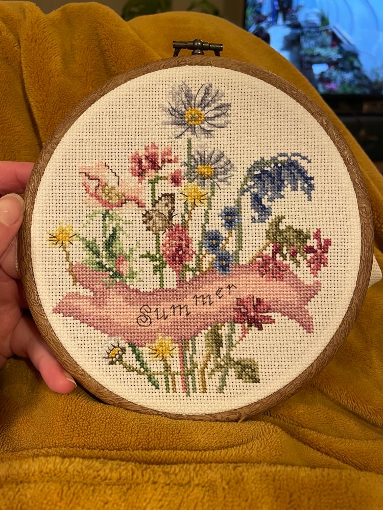 Summer themed cross stitch of some flowers and a pink banner that says summer 