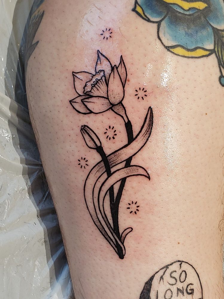 A fresh tattoo of a daffodil and bud. There's a small amount of whip shading, and a few other healed tattoos are visible. 