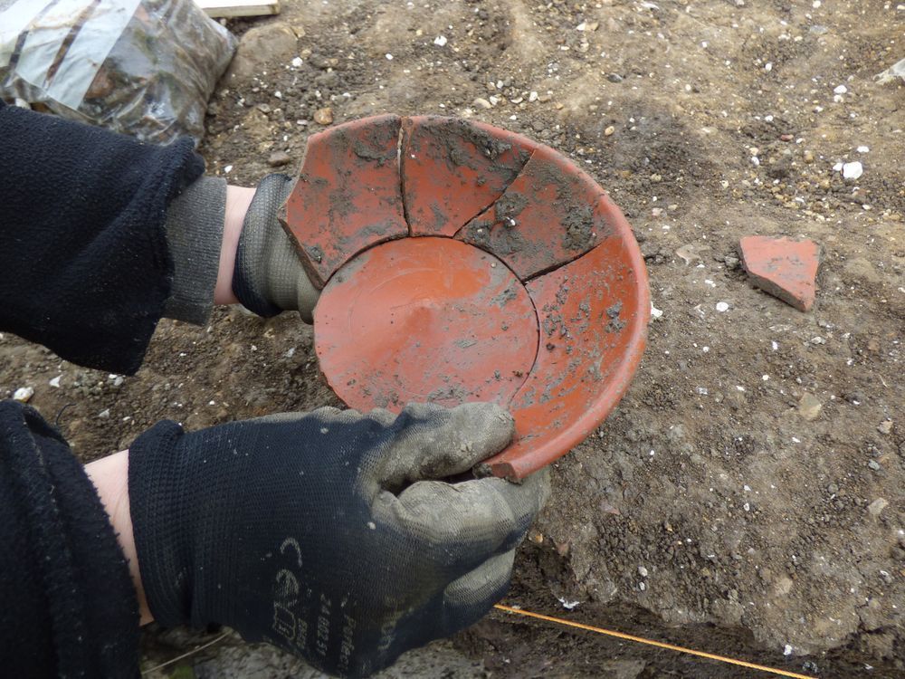 Red ceramic sherds covered in mud, held by an archaeologist on site 