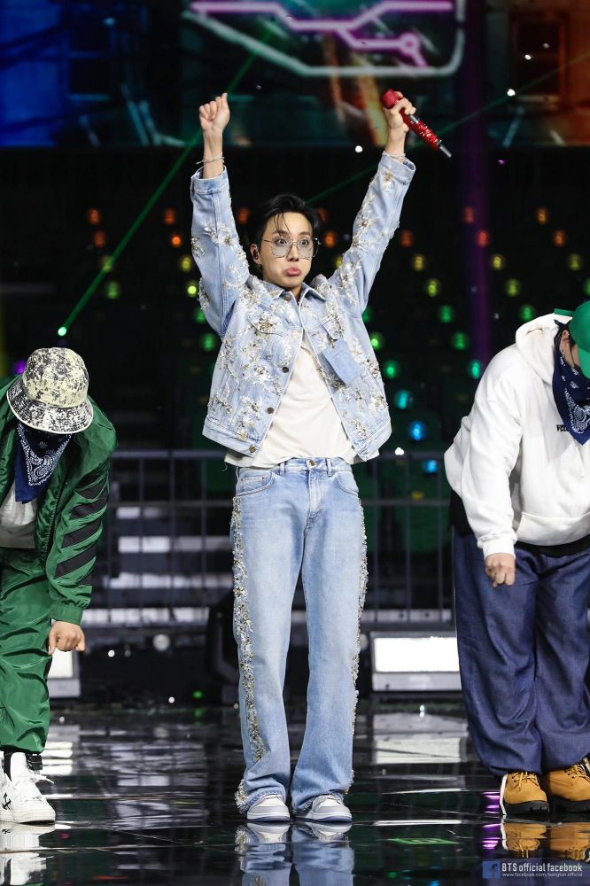 Hoseok in blue jeans, white t-shirt and denim jacket. Dancing Ego with both hands above his head. A huge pout on his face, glasses, red microphone.