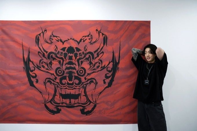 Jungkook standing in front of a red flag with a tiger face on it. FIFA Dreamers in Qatar
