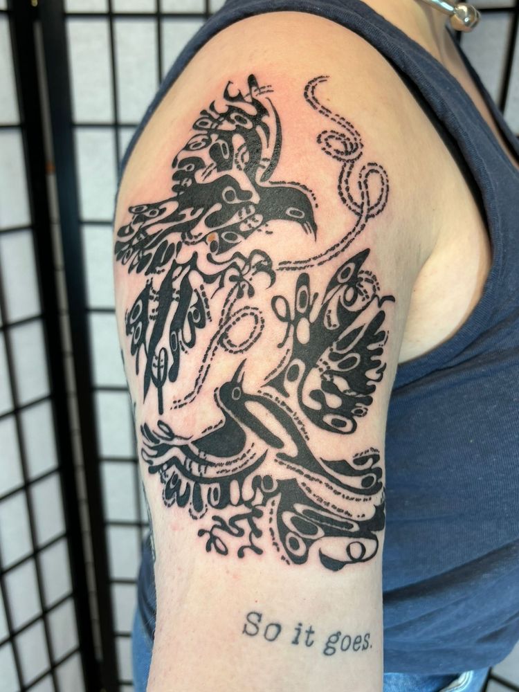 a black tattoo on a woman's upper arm. it shows two magpies circling each other in flight.