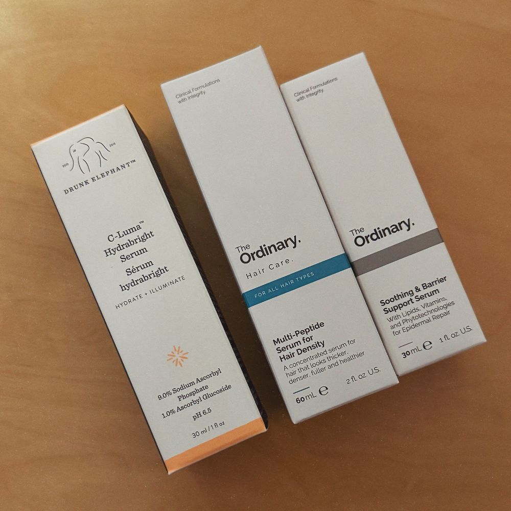 Three bottles of skincare items in their boxes: Drunk Elephant C-Luma, The Ordinary hair density serum and The Ordinary skin barrier support serum. 