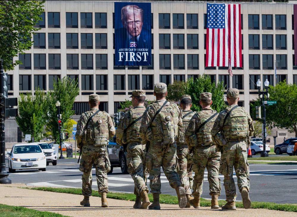 Photo of troops on the streets of Washington DC under a large photo of Trump